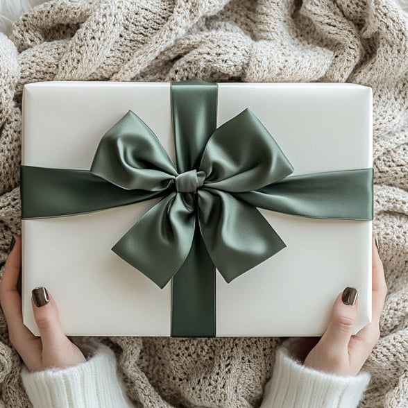 White gift box with a green ribbon held by hands on a textured surface, HEARTICA logo visible